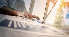 business documents on office table with smart phone and laptop computer and graph business with social network diagram and man working in the background